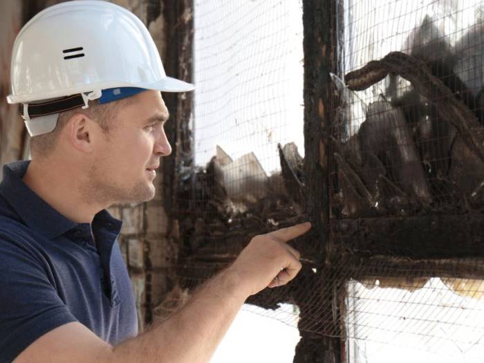 Public adjuster in a hard hat inspecting a fire-damaged window
