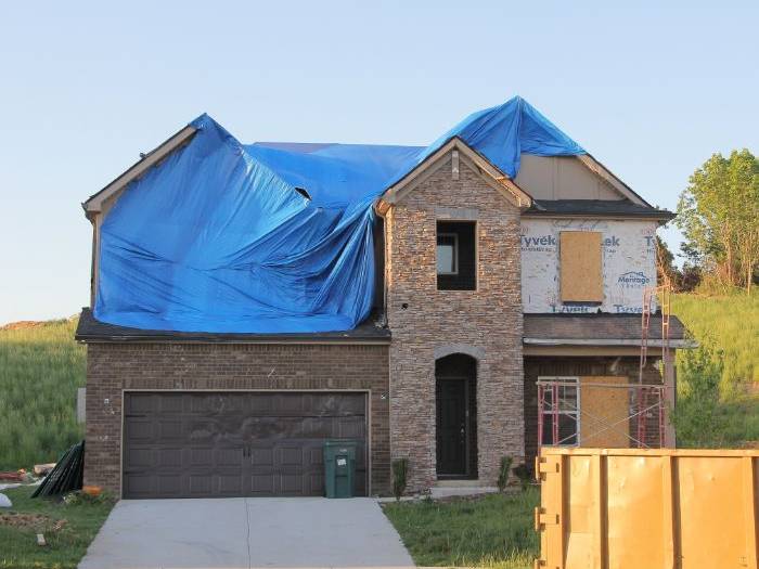 Storm-damaged house with its roof under a blue tarp