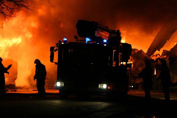 Firefighters and a fire engine in front of a burning building at night